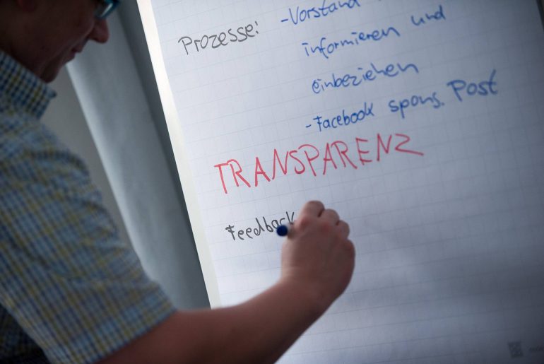 Mensch schreibt "Transparenz" auf ein Flipchart.